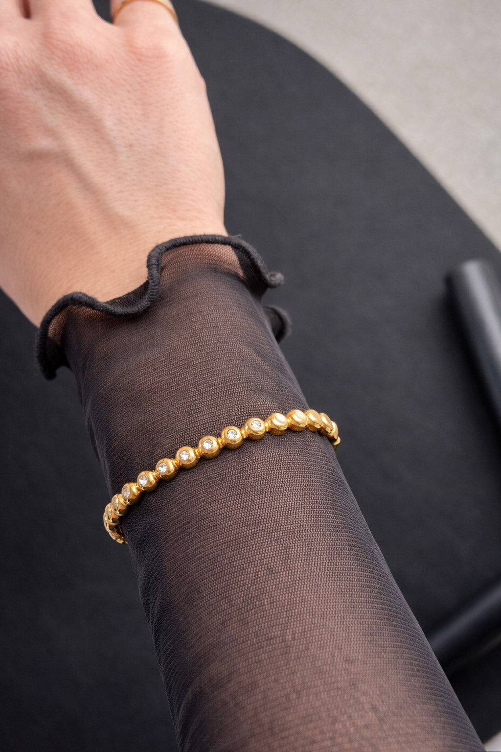 Γυναικείο βραχιόλι χειροπέδα από ατσάλι σε χρυσό χρώμα με πέτρες ζιργκόν φορεμένο