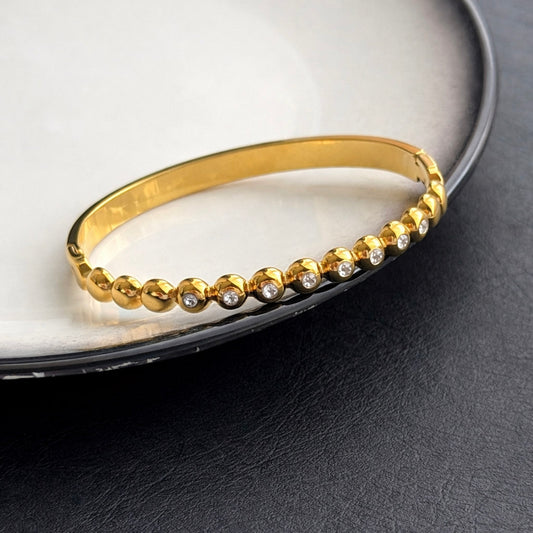 Γυναικείο βραχιόλι χειροπέδα από ατσάλι σε χρυσό χρώμα με πέτρες ζιργκόν close up 