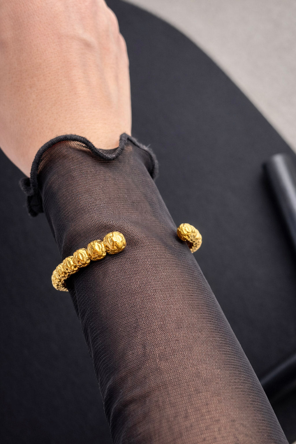 Γυναικείο ανοιχτό βραχιόλι χειροπέδα από ατσάλι σε χρυσό χρώμα με σφυρήλατη υφή φορεμένο